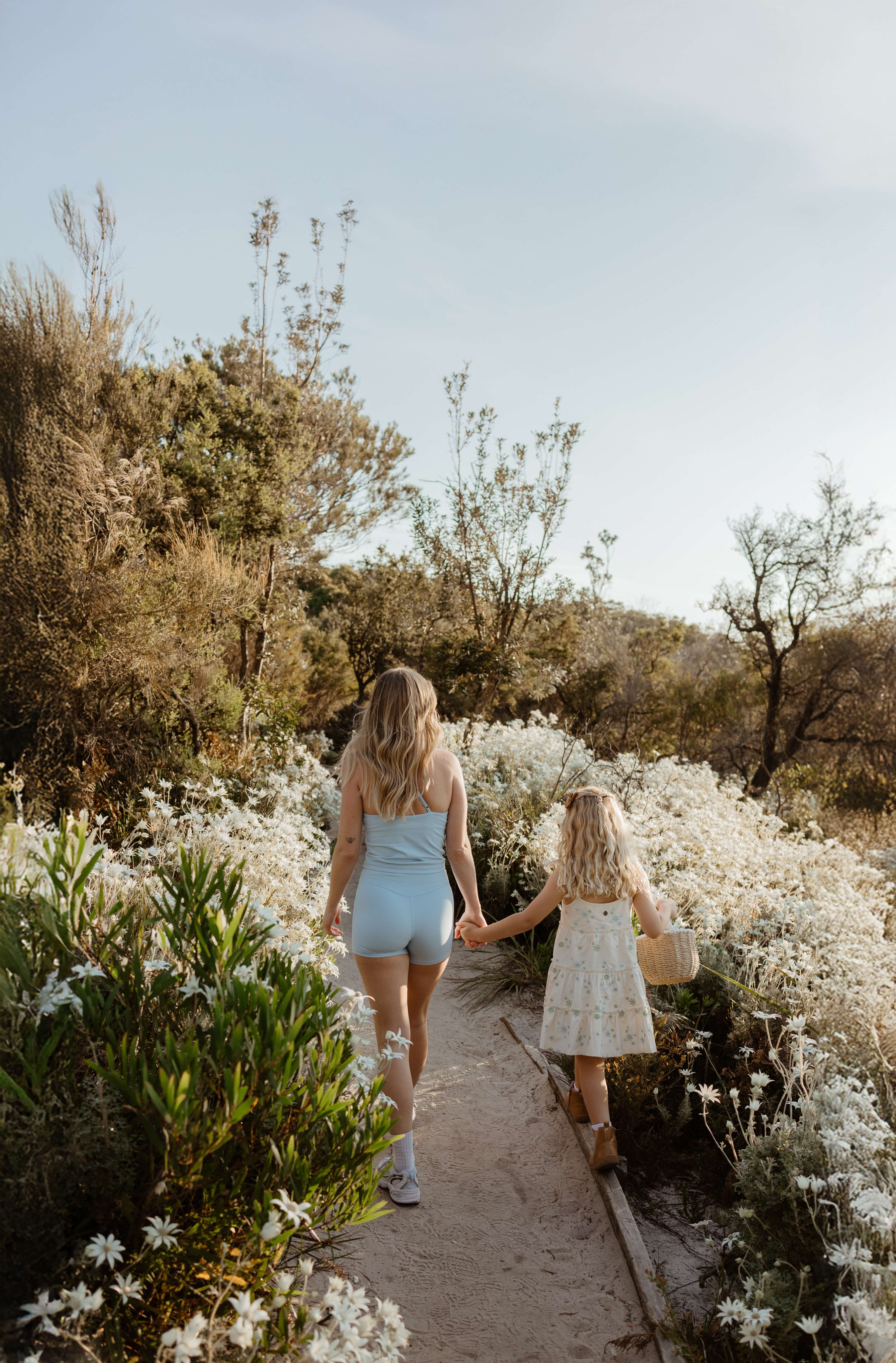 A woman and a child holding hands as they walk along a track filled with wild flannel flowers.