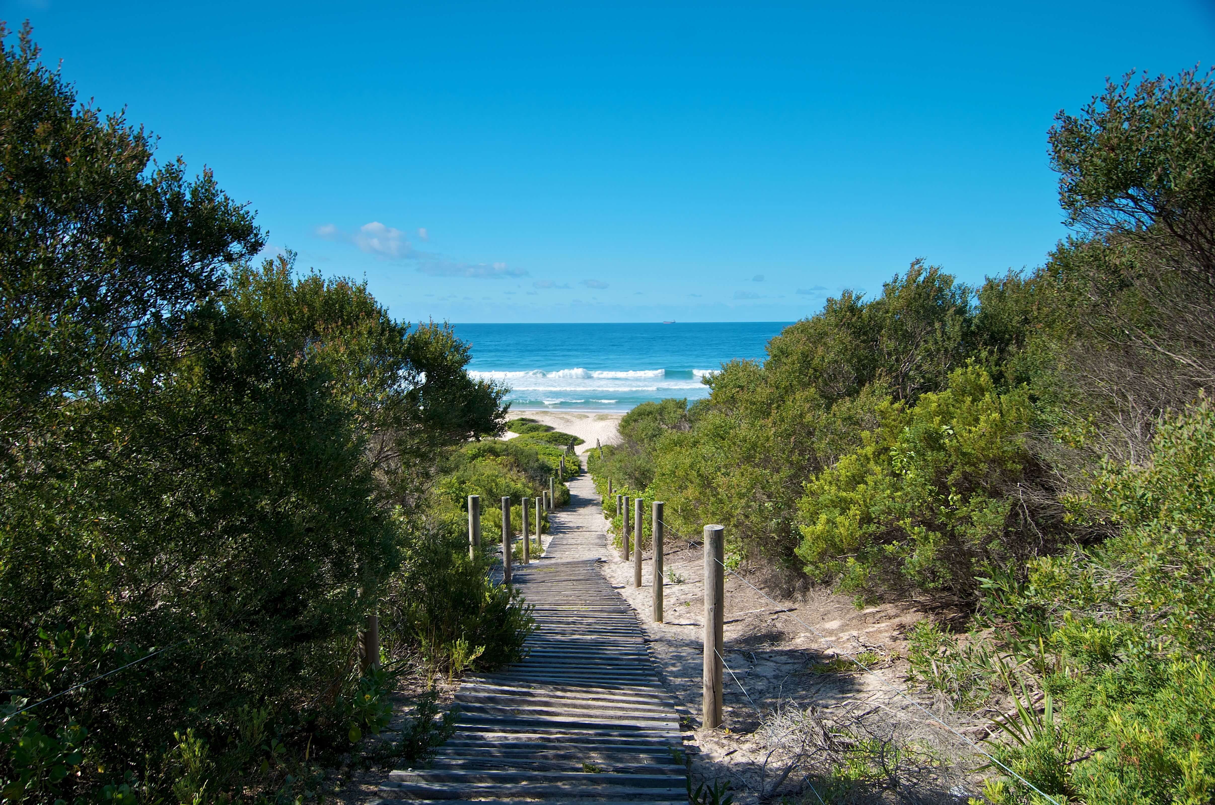 A wooden sandy boardwalk leading to a calm beach