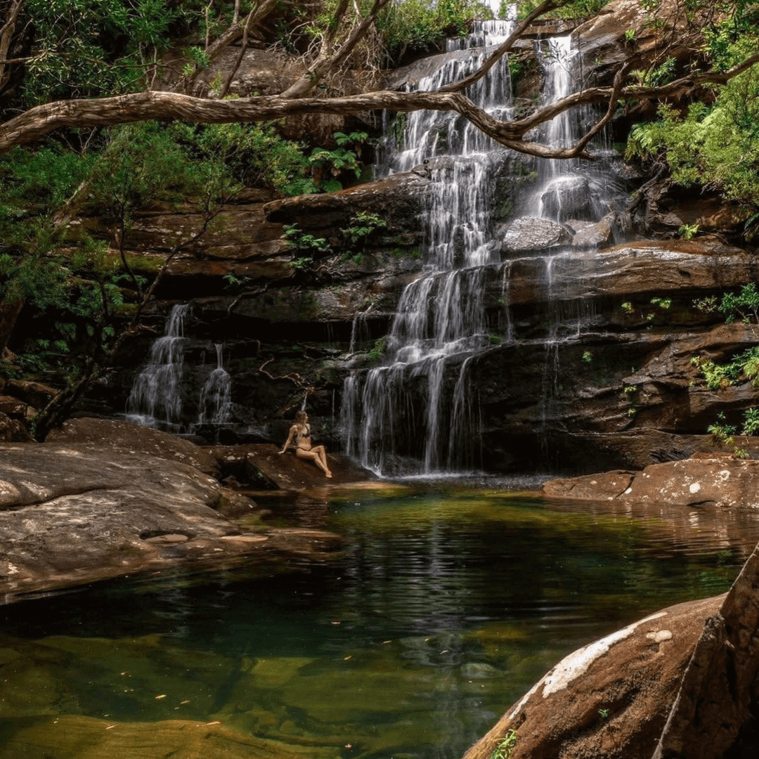 A lady sitting underneath a large waterfall
