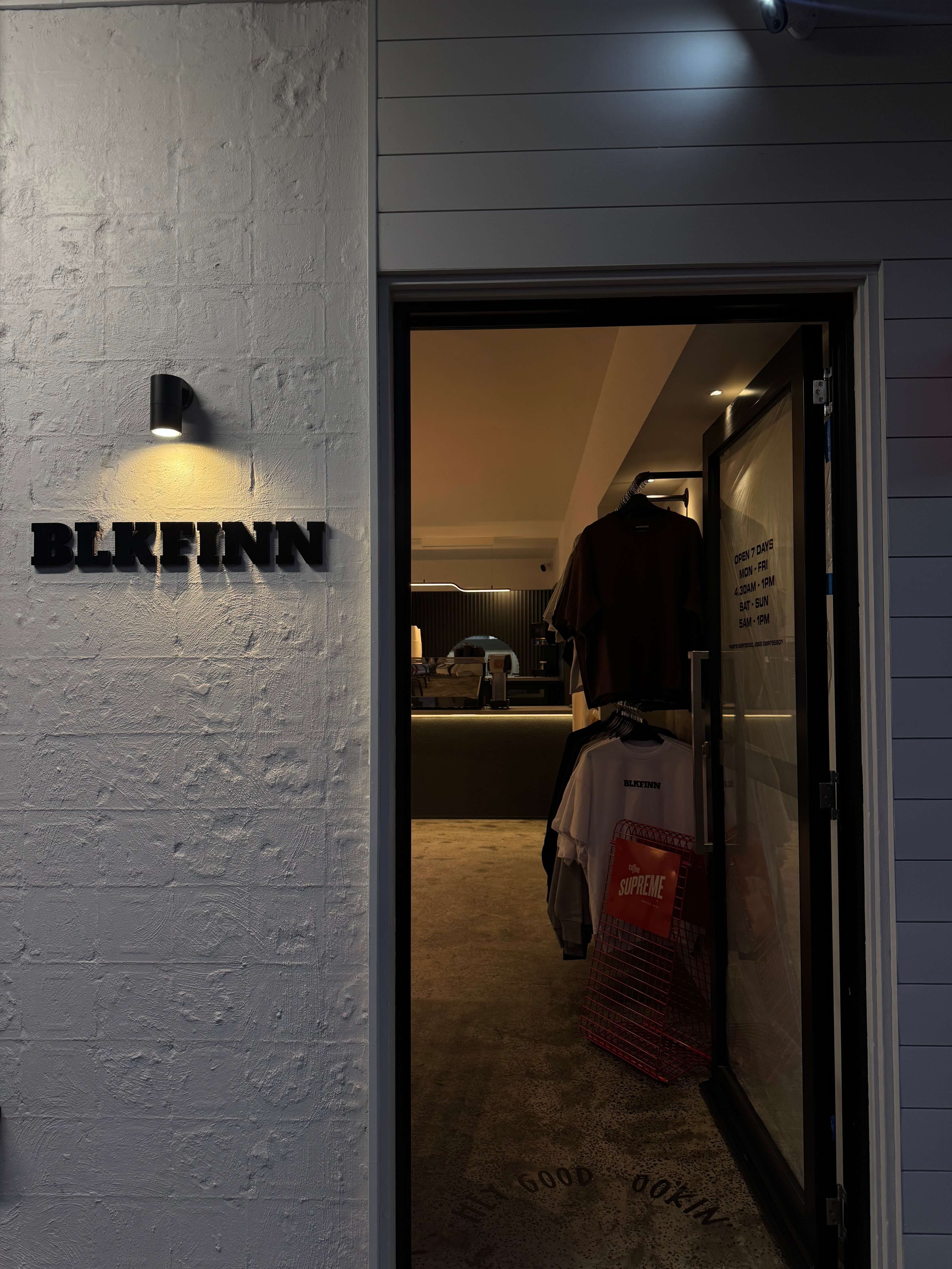 A facade of a white building with a black acrylic sign that says BLKFINN. A rack of clothing can be seen in the background.