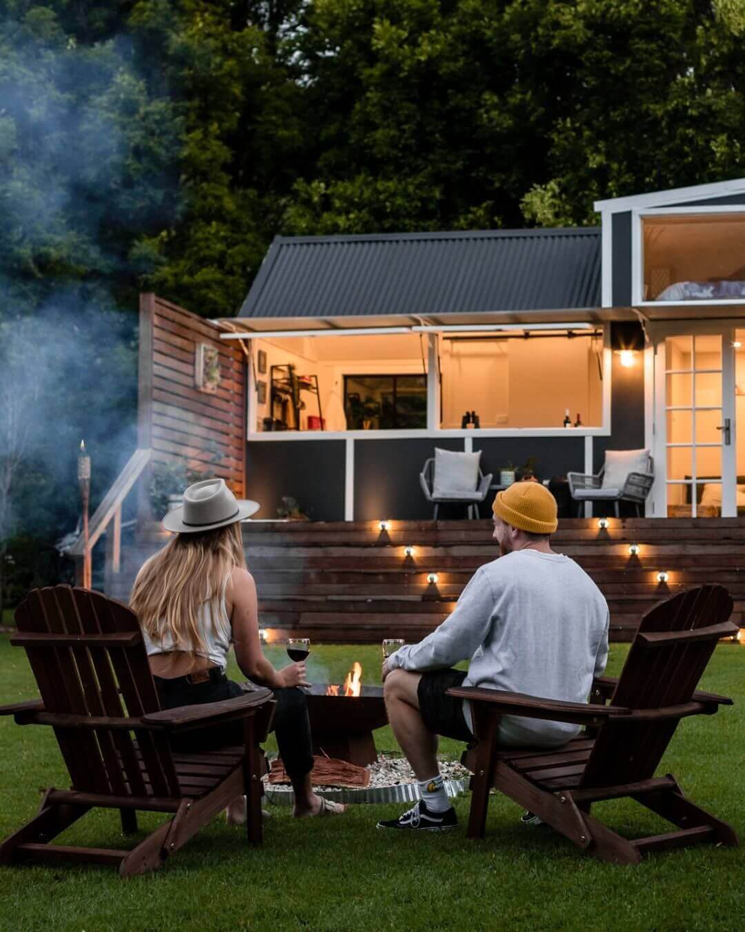 A couple sitting in front of a fire with a tiny home in the background