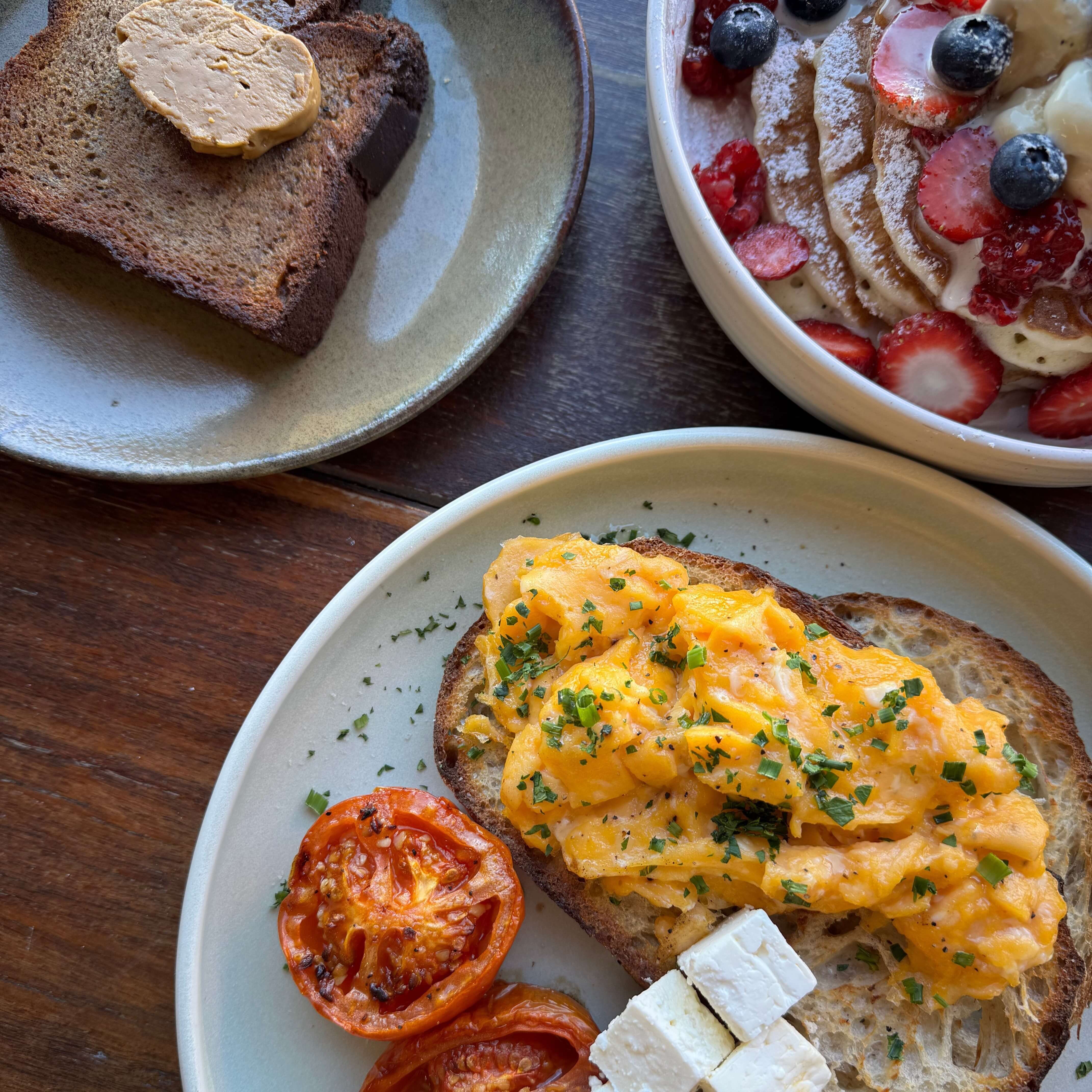 A range of dishes from banana bread, toast with scrambled egg, feta and grilled tomatoes and a plate of pancakes.