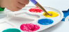A child dips a paintbrush into a paint filled palette