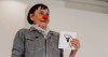 lown performer wearing a red nose striking a playful pose on a bright red chair at the beach, promoting clown workshop with Roundabout Circus Gosford