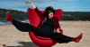 lown Alicia wearing a red nose striking a playful pose on a bright red chair at the beach, promoting clown workshop with Roundabout Circus Gosford